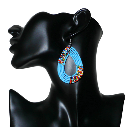 Boucles d'oreilles kenyanes multi-rangs en perles de rocaille bleu ciel et multicolores. Elles mesurent 7 cm de long et 4 cm de large et se portent sur des oreilles percées.