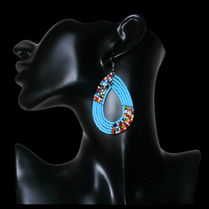 Boucles d'oreilles kenyanes multi-rangs en perles de rocaille bleu ciel et multicolores. Elles mesurent 7 cm de long et 4 cm de large et se portent sur des oreilles percées.