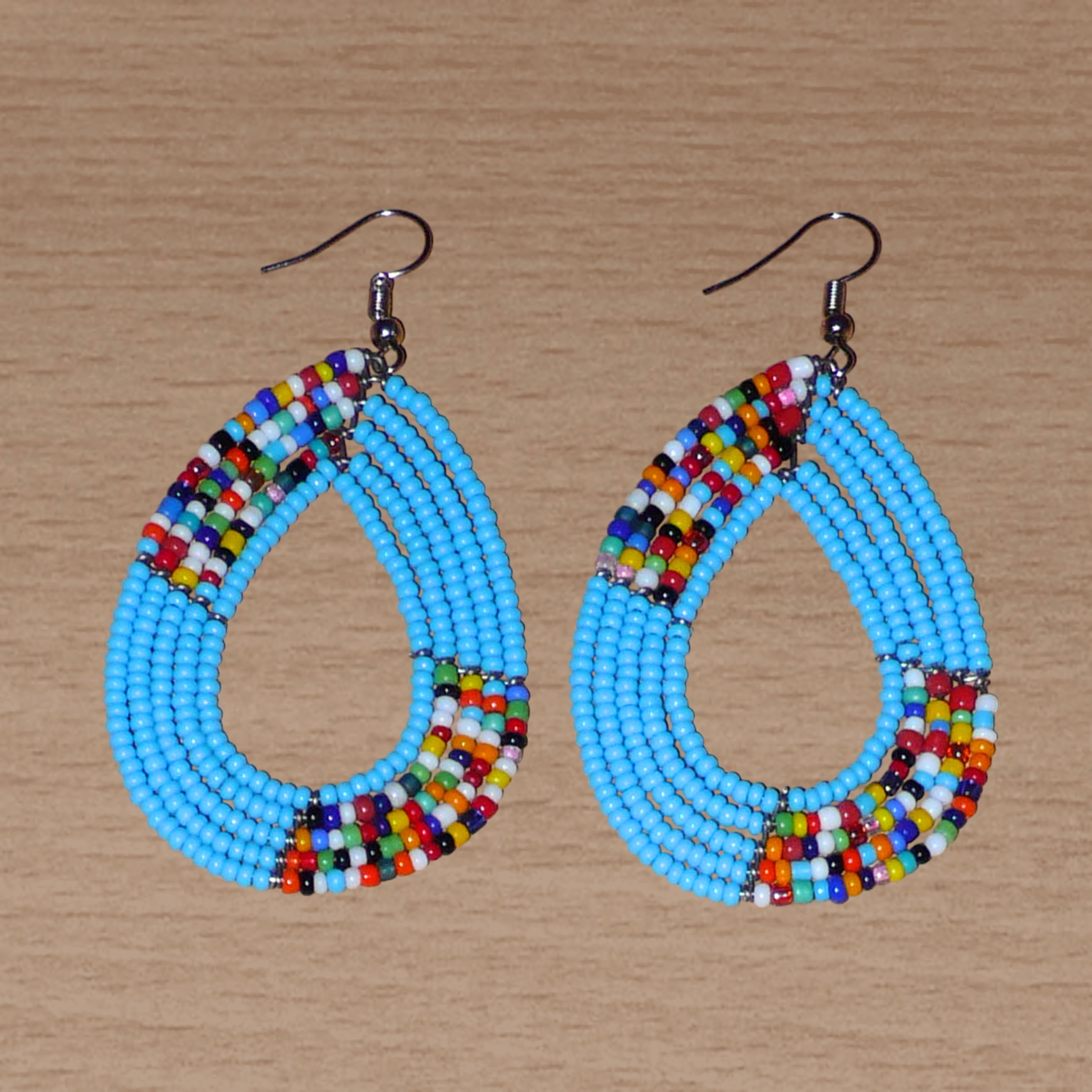 Boucles d'oreilles kenyanes multi-rangs en perles de rocaille bleu ciel et multicolores. Elles mesurent 7 cm de long et 4 cm de large et se portent sur des oreilles percées.
