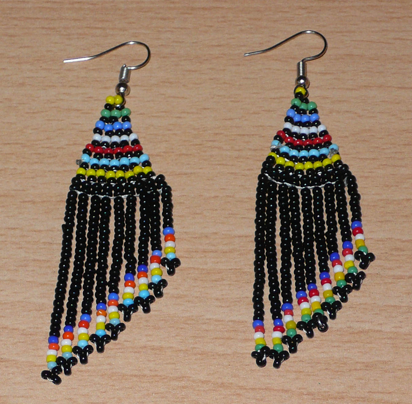 Boucles d'oreilles ethniques sud-africaines à franges asymétriques composées d'un tissage de perles de rocaille noires et multicolores. Elles mesurent 8.5 cm de long et 2 cm de large.