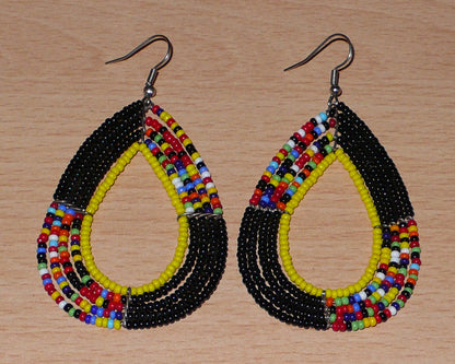 Longues boucles d'oreilles ethniques fabriquée au Kenya faites de perles de rocaille noires, jaunes et multicolores montées en forme de gouttes. Elles mesurent 8,5 cm de long et 4,5 cm de large et se portent avec des crochets en acier inoxydable sur des oreilles percées.