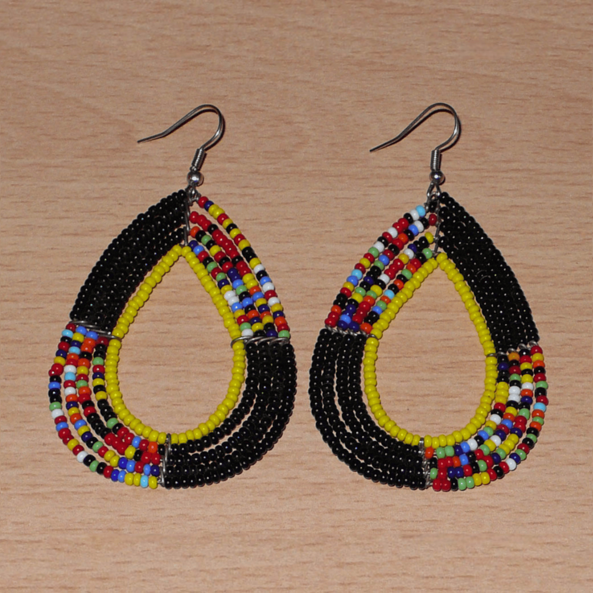Longues boucles d'oreilles ethniques fabriquée au Kenya faites de perles de rocaille noires, jaunes et multicolores montées en forme de gouttes. Elles mesurent 8,5 cm de long et 4,5 cm de large et se portent avec des crochets en acier inoxydable sur des oreilles percées.