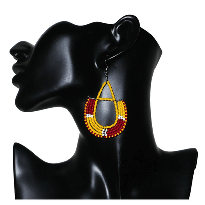 Boucles d'oreilles ethniques tricolores en forme d'ancres composées de perles de rocaille jaunes, rouges et blanches ; elles mesurent 7,5 cm de long et 4 cm de large et se portent avec des crochets en acier inoxydable sur.des oreilles percées.