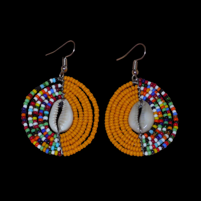 Boucles d'oreilles ethniques orange et multicolores fabriquées au Kenya composées de perles de rocaille et de coquillages cauris. De taille moyenne, elles mesurent 6 cm de long et 3,5 cm de large et se portent sur des oreilles percées.