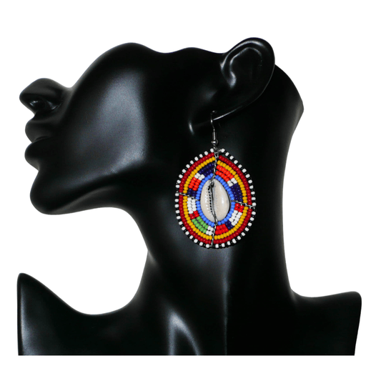 Boucles d'oreilles africaines en forme de boucliers Massai composées de perles multicolores et de coquillages cauris. Ces boucles d'oreilles aux accents ethniques afro chic mesurent 7 cm de long et 4 cm de large et se portent avec des crochets en acier inoxydable sur des oreilles percées. 