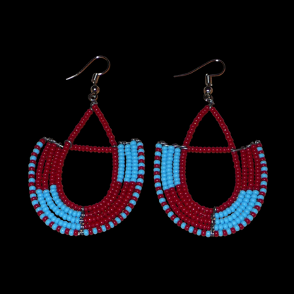 Boucles d'oreilles africaines Massai rouges et bleues composées de perles de rocaille glissées sur des structures géométriques en fils de fer montées en forme d'ancres. Ces boucles d'oreilles bicolores mesurent 7,5 cm de long et 4 cm de large et se portent avec des crochets en acier inoxydable.