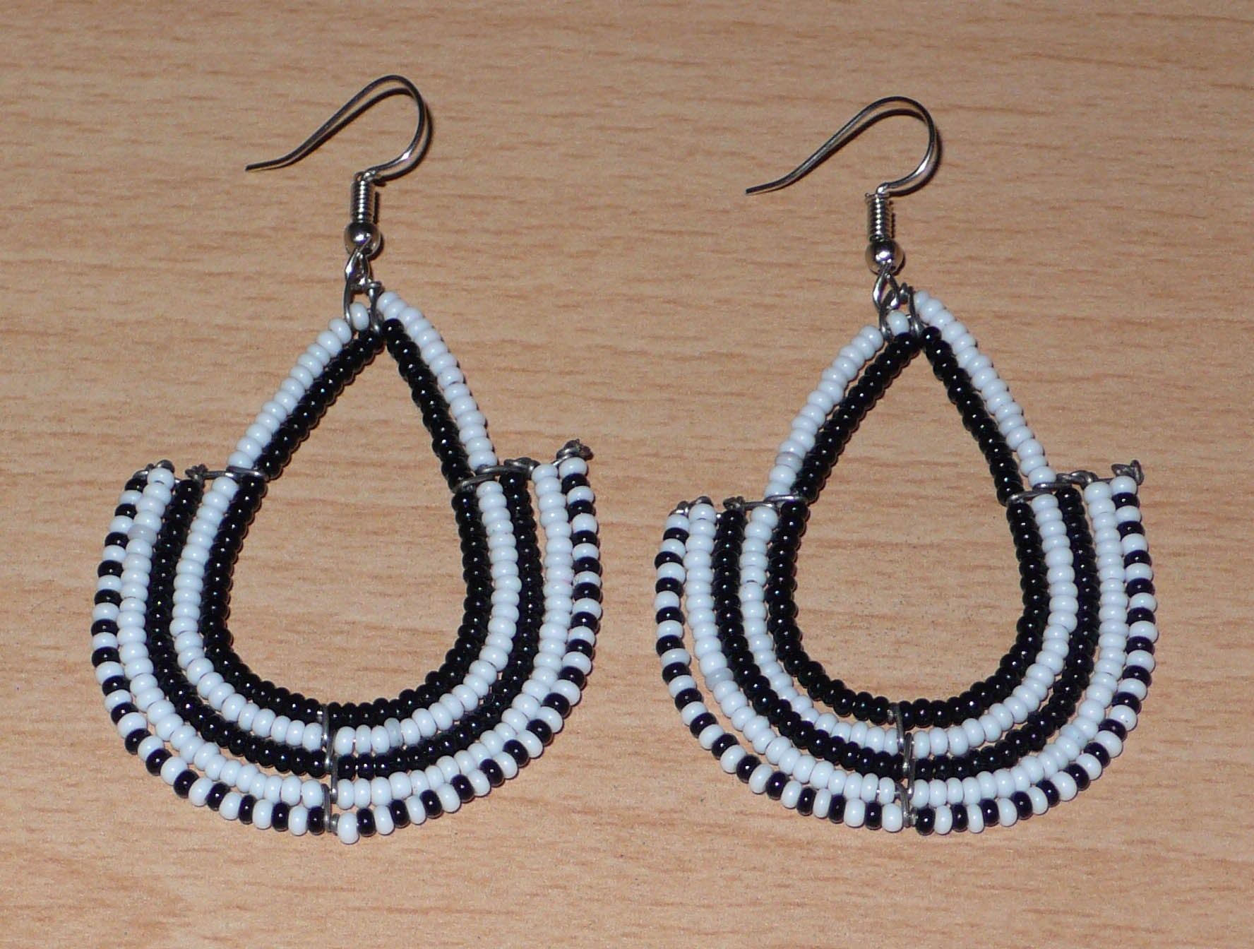 Boucles d'oreilles ethniques bicolores de conception artisanale kenyane : elles se composent de perles de rocaille noires et blanches montées en forme d'ancres. De taille moyenne, cette paire de boucles d'oreilles aux accents ethniques chic mesure 7 cm de long et 4 cm de large, et se porte avec des crochets en acier inoxydable sur des oreilles percées.