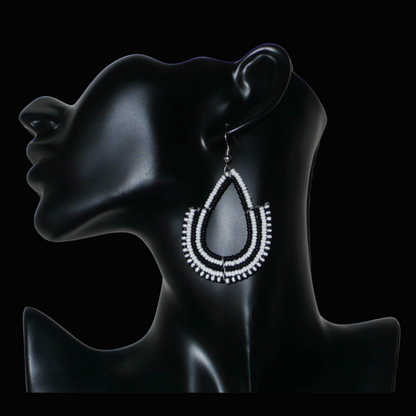 Boucles d'oreilles ethniques bicolores de conception artisanale kenyane : elles se composent de perles de rocaille noires et blanches montées en forme d'ancres. De taille moyenne, cette paire de boucles d'oreilles aux accents ethniques chic mesure 7 cm de long et 4 cm de large, et se porte avec des crochets en acier inoxydable sur des oreilles percées.