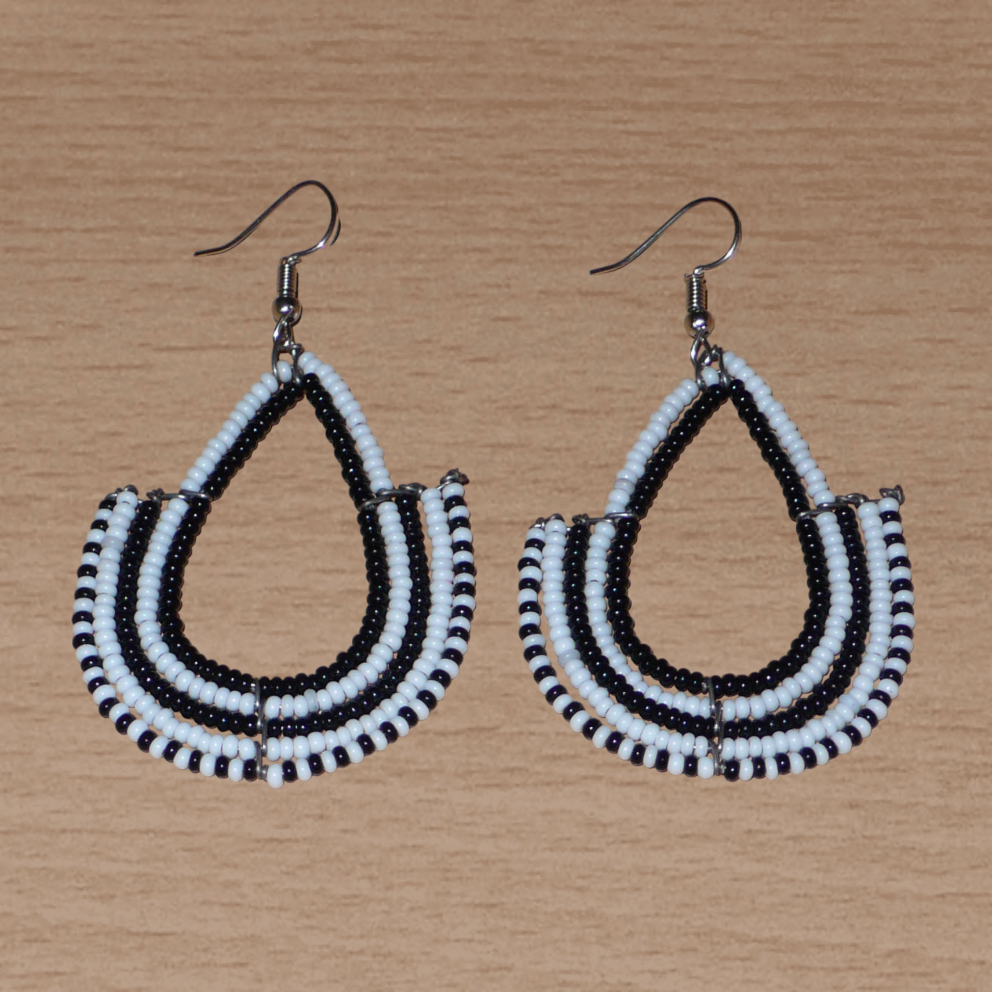 Boucles d'oreilles ethniques bicolores de conception artisanale kenyane : elles se composent de perles de rocaille noires et blanches montées en forme d'ancres. De taille moyenne, cette paire de boucles d'oreilles aux accents ethniques chic mesure 7 cm de long et 4 cm de large, et se porte avec des crochets en acier inoxydable sur des oreilles percées.