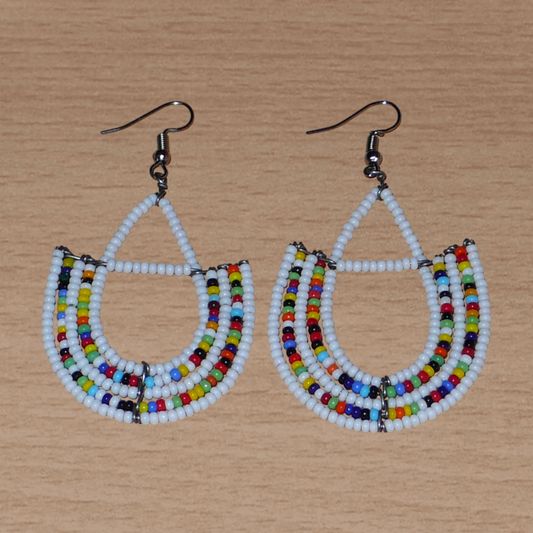 Boucles d'oreilles ethniques blanches et multicolores composées de perles de rocaille montées en forme d'ancres. Ces boucles d'oreilles mesurent 7 cm de long et 4 cm de large ; elles se portent avec des crochets en acier inoxydable sur des oreilles percées.
