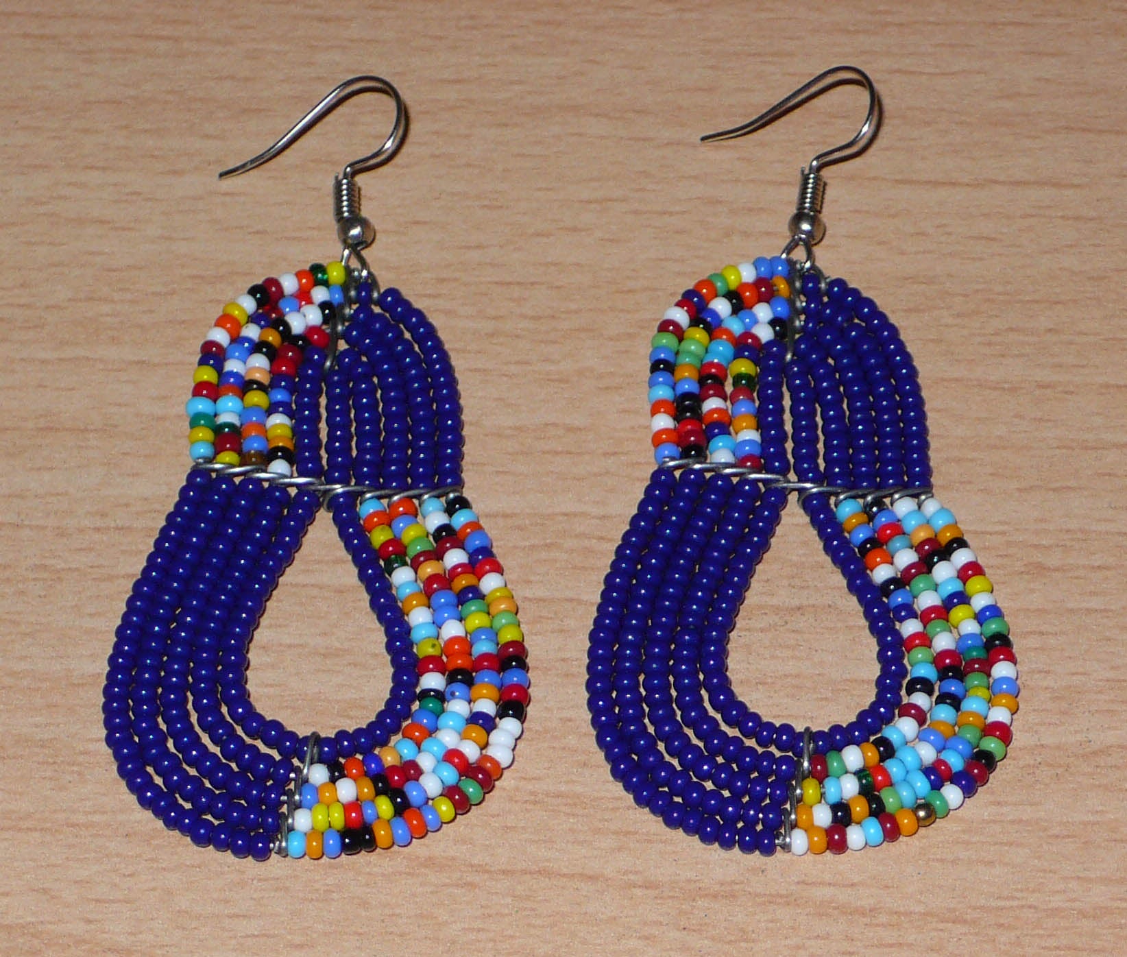 Boucles d'oreilles ethniques bleu marine et multicolores : de fabrication artisanale kenyane Massai, elles se composent de perles de rocaille glissées sur plusieurs rangées de fils de fer. Ces boucles d'oreilles aux accents afro bohème mesurent 8 cm de long et 3.5 cm de large, et se portent avec des crochets en acier inoxydable sur des oreilles percées.