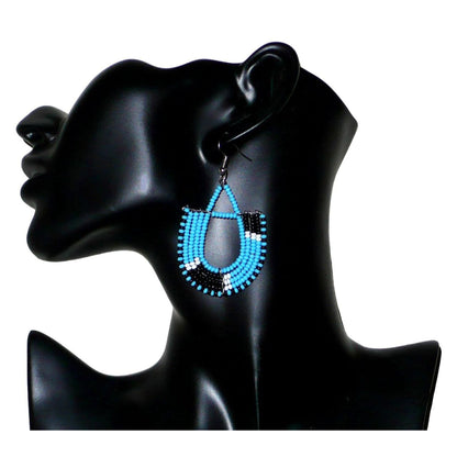Boucles d'oreilles ethniques tricolores en forme d'ancres composées de perles bleues, noires et blanches. Elles mesurent 7 cm de long et 4 cm de large et se portent sur des oreilles percées.