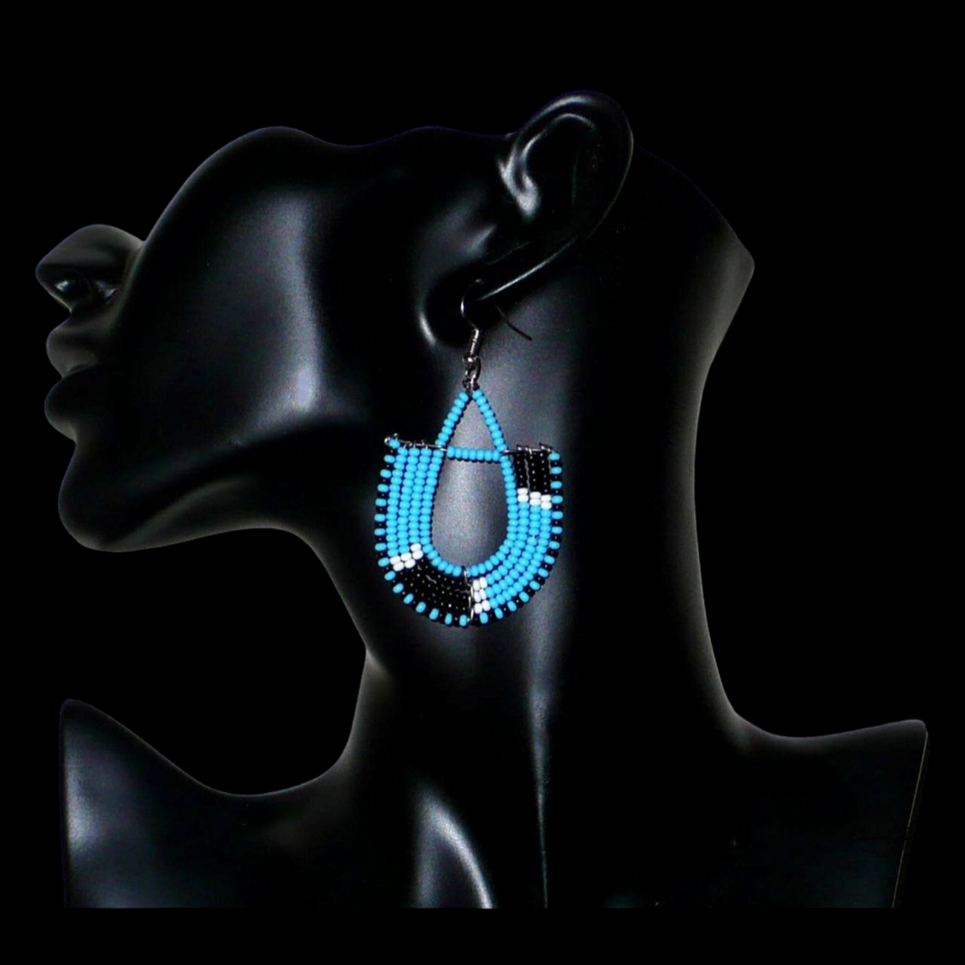 Boucles d'oreilles ethniques tricolores en forme d'ancres composées de perles bleues, noires et blanches. Elles mesurent 7 cm de long et 4 cm de large et se portent sur des oreilles percées.
