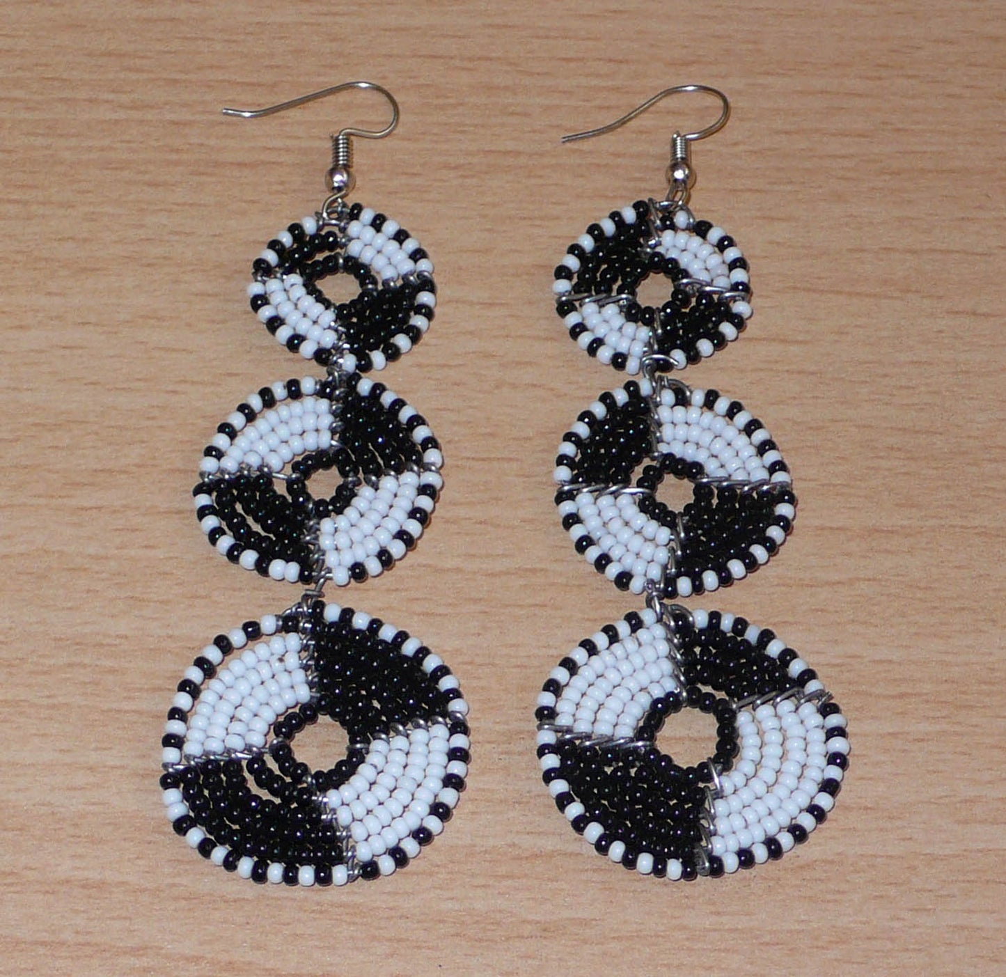 Longues boucles d'oreilles ethniques Massai composées de perles noires et blanches montées en cercles superposés. Ces boucles d'oreilles bicolores mesurent 9,5 cm de long et 3 cm de large ; elles se portent avec des crochets sur des oreilles percées.
