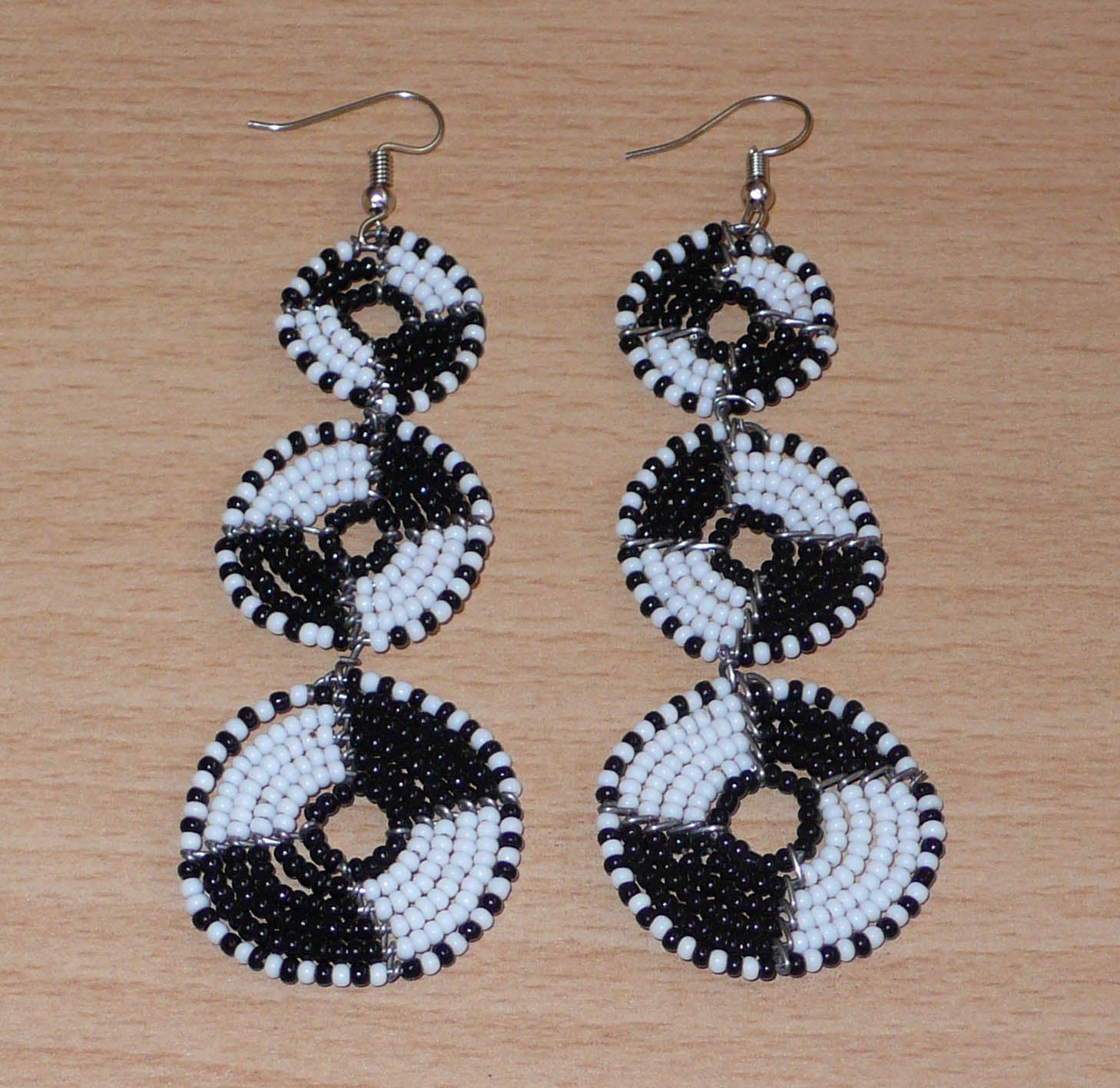 Longues boucles d'oreilles ethniques Massai composées de perles noires et blanches montées en cercles superposés. Ces boucles d'oreilles bicolores mesurent 9,5 cm de long et 3 cm de large ; elles se portent avec des crochets sur des oreilles percées.