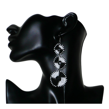 Longues boucles d'oreilles ethniques Massai composées de perles noires et blanches montées en cercles superposés. Ces boucles d'oreilles bicolores mesurent 9,5 cm de long et 3 cm de large ; elles se portent avec des crochets sur des oreilles percées.