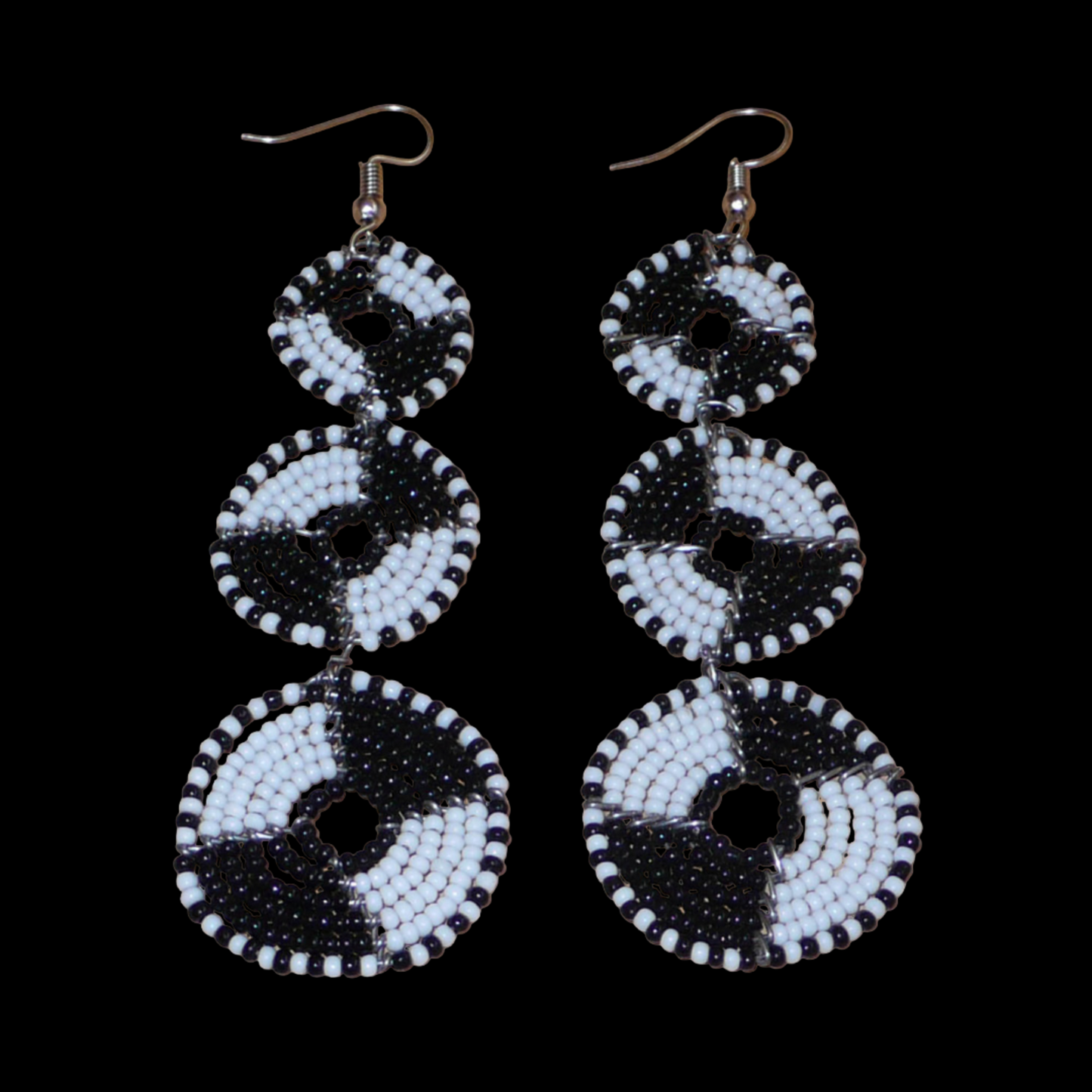 Longues boucles d'oreilles ethniques Massai composées de perles noires et blanches montées en cercles superposés. Ces boucles d'oreilles bicolores mesurent 9,5 cm de long et 3 cm de large ; elles se portent avec des crochets sur des oreilles percées.