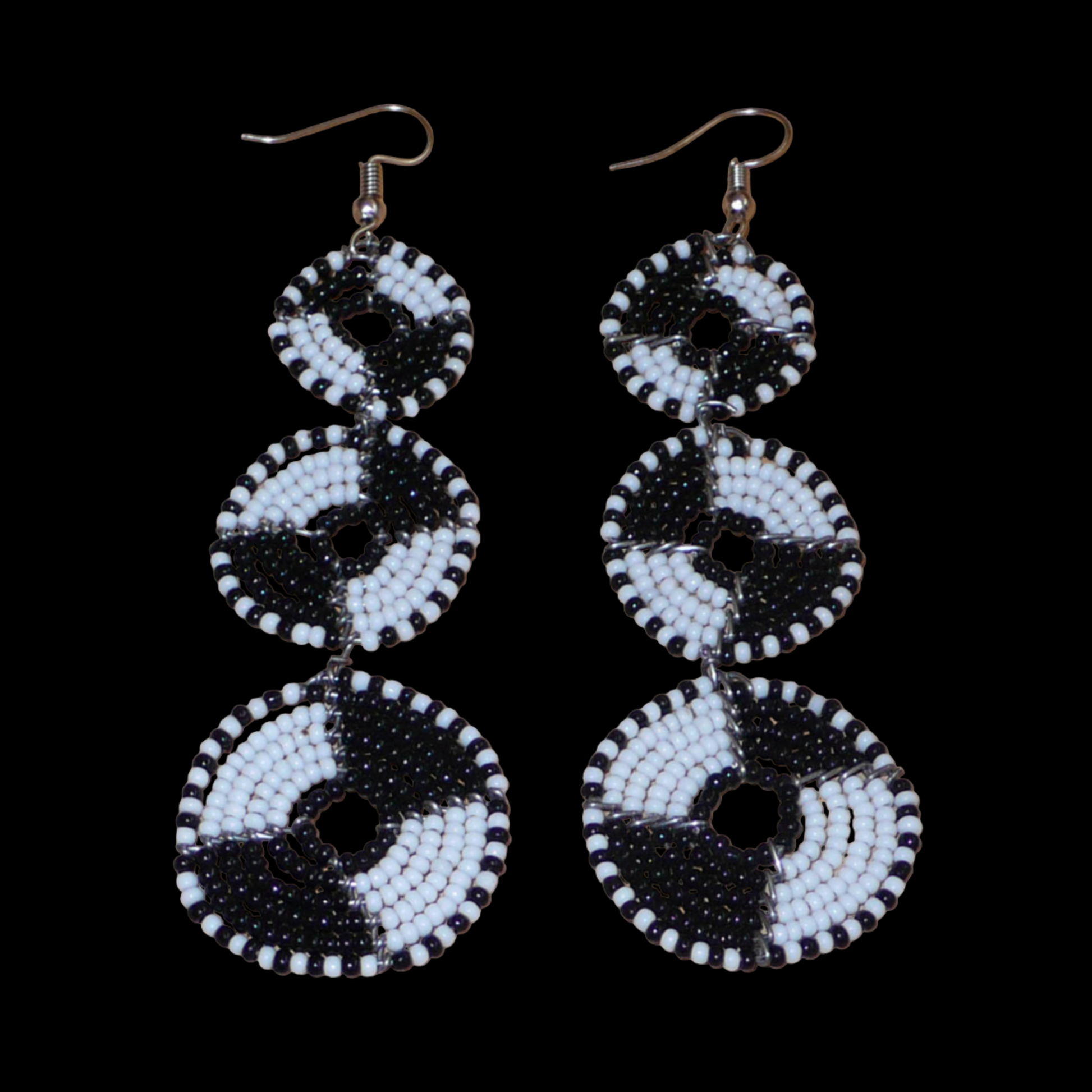 Longues boucles d'oreilles ethniques Massai composées de perles noires et blanches montées en cercles superposés. Ces boucles d'oreilles bicolores mesurent 9,5 cm de long et 3 cm de large ; elles se portent avec des crochets sur des oreilles percées.