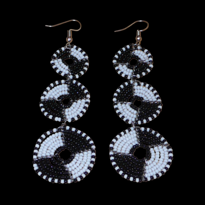 Longues boucles d'oreilles ethniques Massai composées de perles noires et blanches montées en cercles superposés. Ces boucles d'oreilles bicolores mesurent 9,5 cm de long et 3 cm de large ; elles se portent avec des crochets sur des oreilles percées.