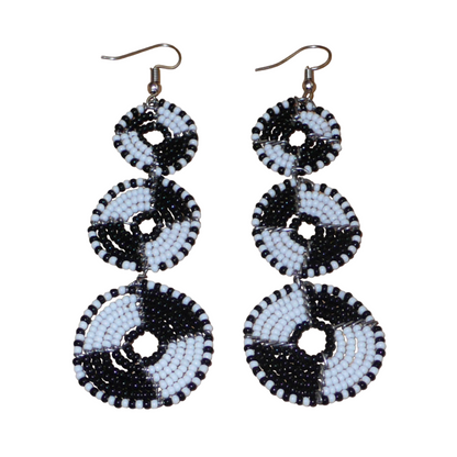 Longues boucles d'oreilles ethniques Massai composées de perles noires et blanches montées en cercles superposés. Ces boucles d'oreilles bicolores mesurent 9,5 cm de long et 3 cm de large ; elles se portent avec des crochets sur des oreilles percées.