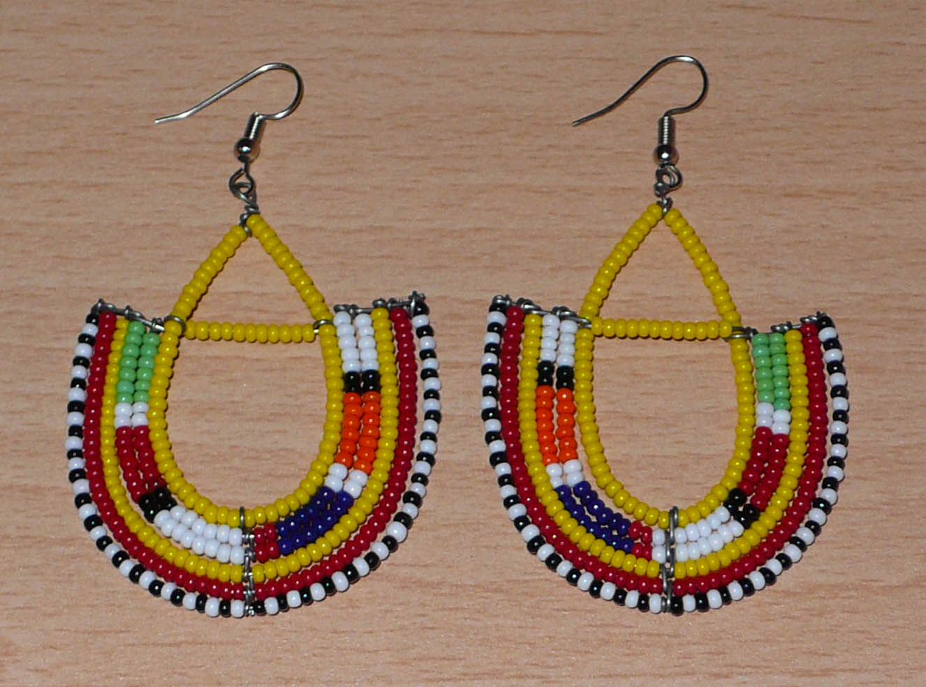Boucles d'oreilles africaines traditionnelles aux couleurs ethniques et motifs Massai rappelant le style afro chic des années 70 : elles se composent de perles de rocaille jaunes et multicolores fixées sur des structures en fils de fer en forme d'ancres. Elles mesurent 7.5 cm de long et 4.5 cm de large, elles se portent avec des crochets en acier inoxydable sur des oreilles percées.