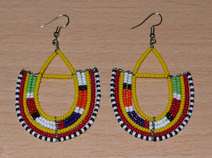 Boucles d'oreilles africaines traditionnelles aux couleurs ethniques et motifs Massai rappelant le style afro chic des années 70 : elles se composent de perles de rocaille jaunes et multicolores fixées sur des structures en fils de fer en forme d'ancres. Elles mesurent 7.5 cm de long et 4.5 cm de large, elles se portent avec des crochets en acier inoxydable sur des oreilles percées.
