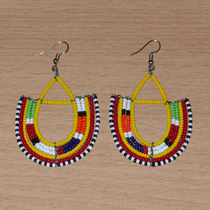 Boucles d'oreilles africaines traditionnelles aux couleurs ethniques et motifs Massai rappelant le style afro chic des années 70 : elles se composent de perles de rocaille jaunes et multicolores fixées sur des structures en fils de fer en forme d'ancres. Elles mesurent 7.5 cm de long et 4.5 cm de large, elles se portent avec des crochets en acier inoxydable sur des oreilles percées.