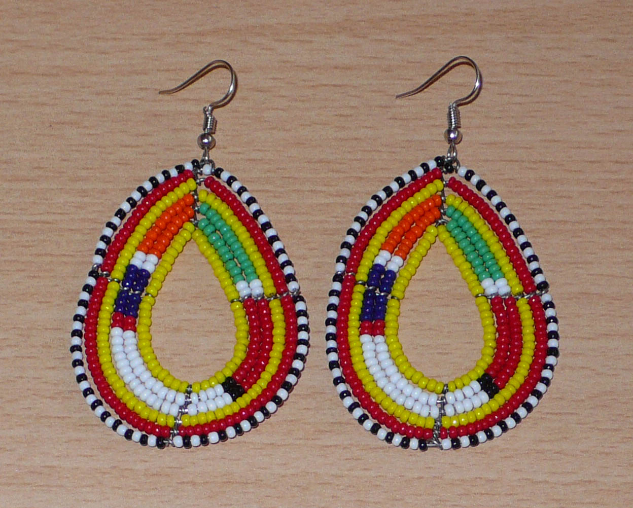 Boucles d'oreilles ethniques de tradition Massai en forme de gouttes faites de perles de rocaille jaunes et multicolores. Elles mesurent 8 cm de long et 4 cm de large et se portent avec des crochets en acier inoxydable sur des oreilles percées. 