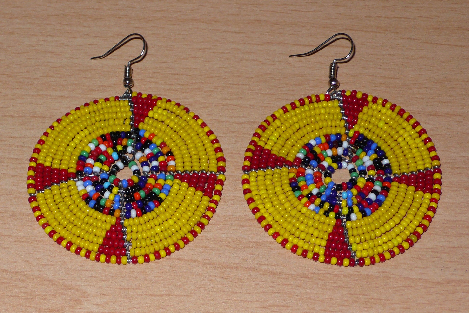 Boucles d'oreilles ethniques kenyanes en perles de rocaille principalement jaunes, puis rouges et multicolores enfilées sur des structures circulaires en fils de fer. Elles mesurent 7.5 cm de long et se portent sur des oreilles percées.