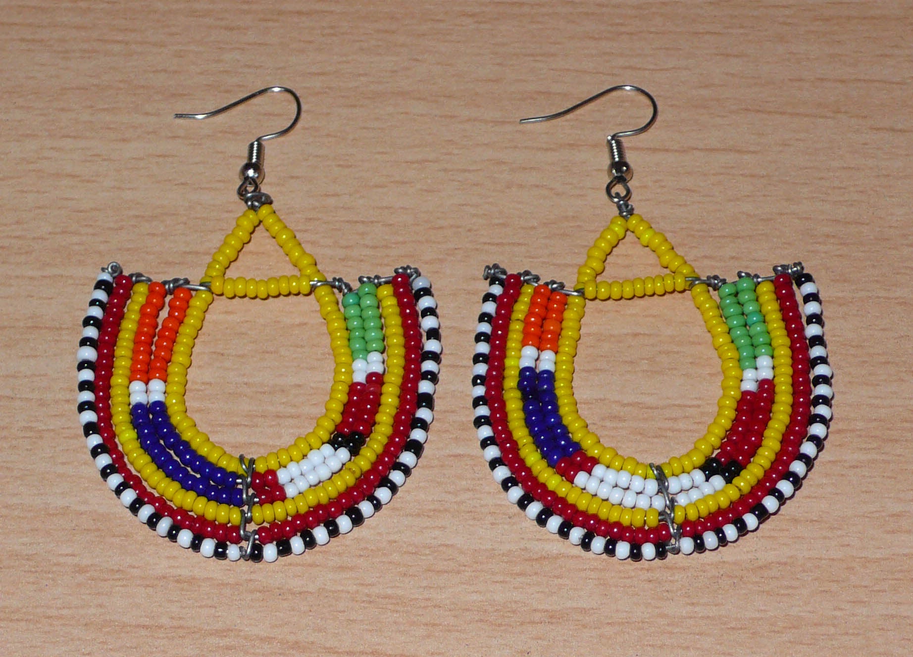 Cette paire de boucles d'oreilles africaines traditionnelles, de fabrication artisanale Massai, apportera une touche ethnique à votre look ! Ces boucles d'oreilles aux accents exotiques se composent de perles de rocaille jaunes et multicolores glissées sur des fils de fer montés en forme d'ancres. Elles mesurent 7 cm de long et 4.5 cm de large, et se portent avec des crochets en acier inoxydable sur des oreilles percées.