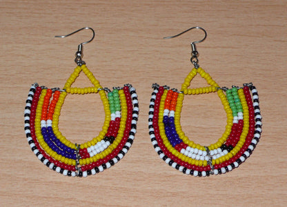 Cette paire de boucles d'oreilles africaines traditionnelles, de fabrication artisanale Massai, apportera une touche ethnique à votre look ! Ces boucles d'oreilles aux accents exotiques se composent de perles de rocaille jaunes et multicolores glissées sur des fils de fer montés en forme d'ancres. Elles mesurent 7 cm de long et 4.5 cm de large, et se portent avec des crochets en acier inoxydable sur des oreilles percées.
