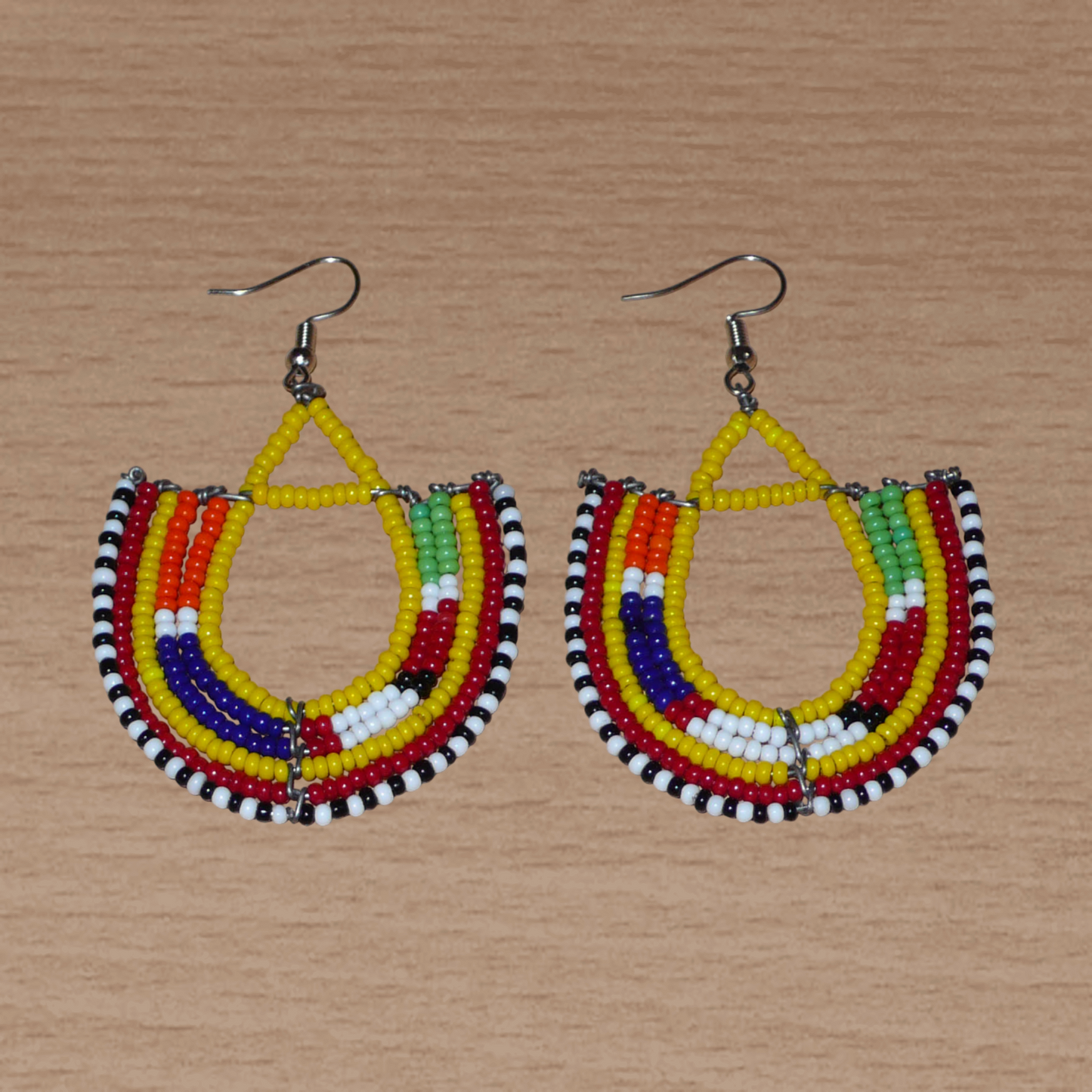 Cette paire de boucles d'oreilles africaines traditionnelles, de fabrication artisanale Massai, apportera une touche ethnique à votre look ! Ces boucles d'oreilles aux accents exotiques se composent de perles de rocaille jaunes et multicolores glissées sur des fils de fer montés en forme d'ancres. Elles mesurent 7 cm de long et 4.5 cm de large, et se portent avec des crochets en acier inoxydable sur des oreilles percées.