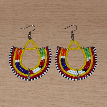 Cette paire de boucles d'oreilles africaines traditionnelles, de fabrication artisanale Massai, apportera une touche ethnique à votre look ! Ces boucles d'oreilles aux accents exotiques se composent de perles de rocaille jaunes et multicolores glissées sur des fils de fer montés en forme d'ancres. Elles mesurent 7 cm de long et 4.5 cm de large, et se portent avec des crochets en acier inoxydable sur des oreilles percées.