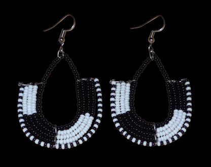 Boucles d'oreilles ethniques bicolores en forme d'ancres composées de perles de rocaille noires et blanches glissées sur des structures géométriques en fils de fer. De taille moyenne, ces boucles d'oreilles aux accents afro chic mesurent 7 cm de long et 4 cm de large ; elles se portent avec des crochets en acier inoxydable sur des oreilles percées.