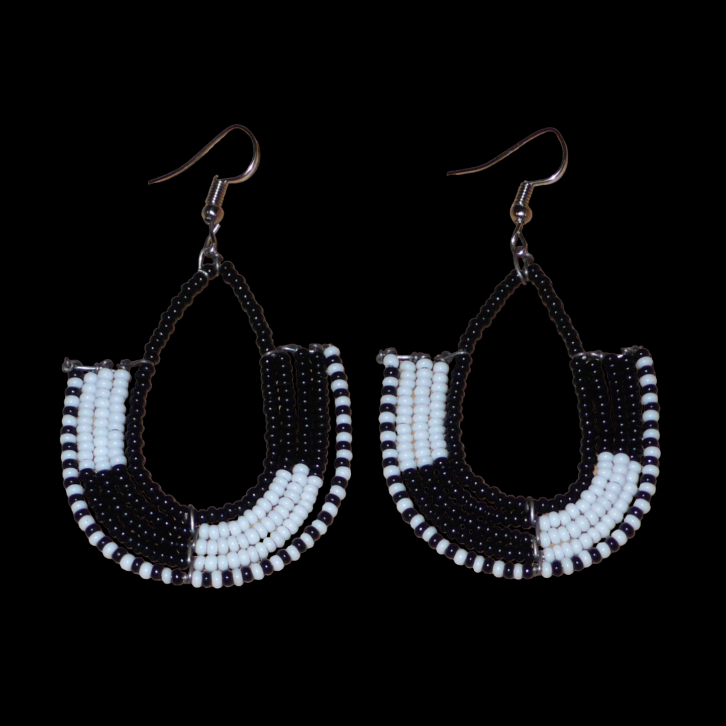 Boucles d'oreilles ethniques bicolores en forme d'ancres composées de perles de rocaille noires et blanches glissées sur des structures géométriques en fils de fer. De taille moyenne, ces boucles d'oreilles aux accents afro chic mesurent 7 cm de long et 4 cm de large ; elles se portent avec des crochets en acier inoxydable sur des oreilles percées.