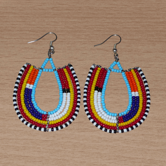 Boucles d'oreilles africaines traditionnelles Massai en forme d'ancres composées de perles de rocaille bleues et multicolores glissées sur des structures géométriques en fils de fer. Elles mesurent 8 cm de long et 4.5 cm de large, et se portent avec des crochets en acier inoxydable sur des oreilles percées. 