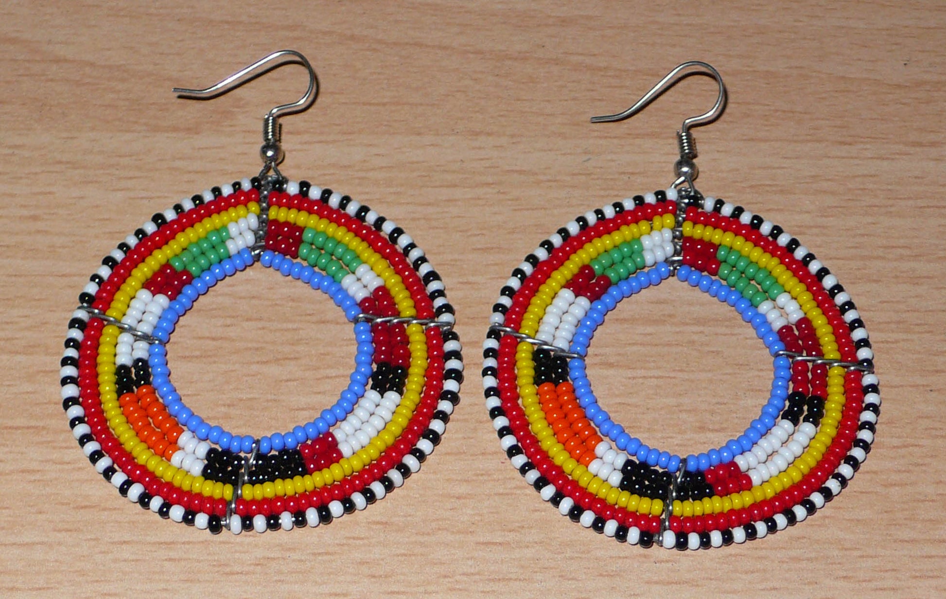 Boucles d'oreilles africaines rondes traditionnelles à motifs ethniques Massai composées de perles de rocaille bleues et multicolores. Ces créoles perlées mesurent 7 cm de long et 5 cm de large ; elles se portent avec des crochets en acier inoxydable sur des oreilles percées.