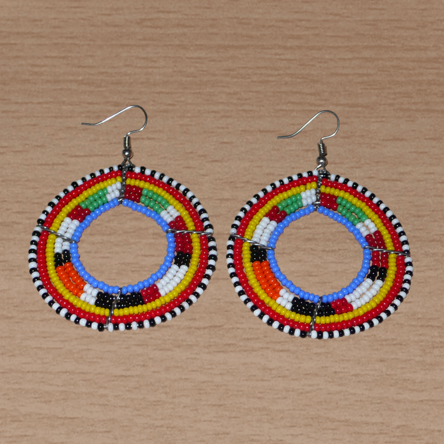 Boucles d'oreilles africaines rondes traditionnelles à motifs ethniques Massai composées de perles de rocaille bleues et multicolores. Ces créoles perlées mesurent 7 cm de long et 5 cm de large ; elles se portent avec des crochets en acier inoxydable sur des oreilles percées.