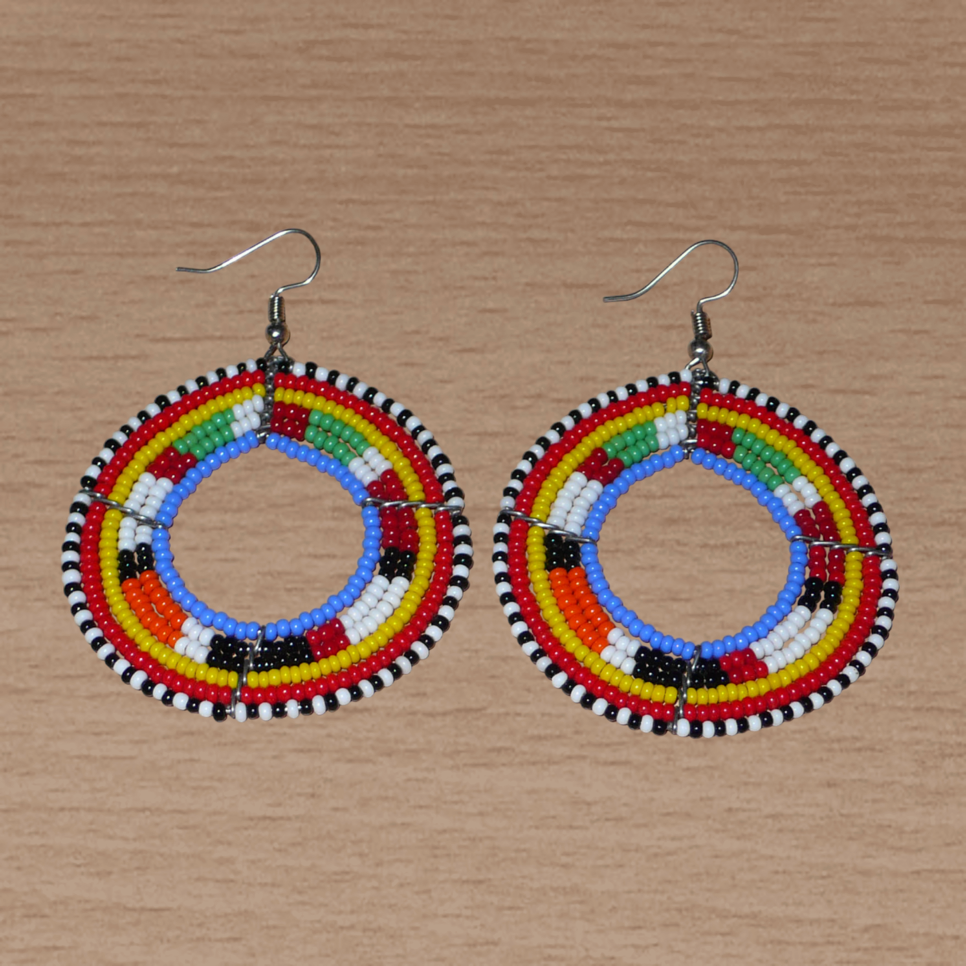 Boucles d'oreilles africaines rondes traditionnelles à motifs ethniques Massai composées de perles de rocaille bleues et multicolores. Ces créoles perlées mesurent 7 cm de long et 5 cm de large ; elles se portent avec des crochets en acier inoxydable sur des oreilles percées.