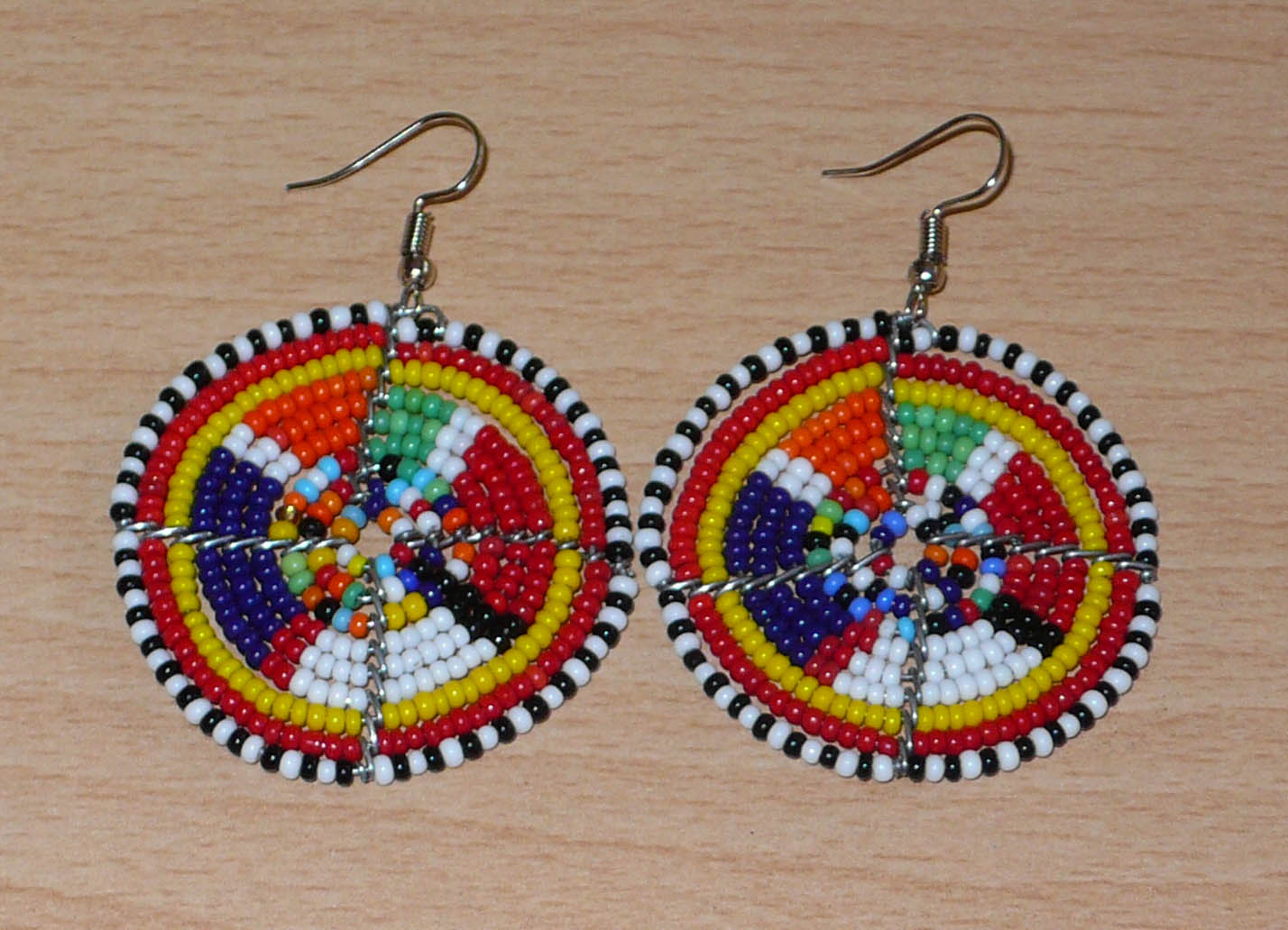 Boucles d'oreilles africaines rondes à motifs ethniques Massai en perles de rocaille multicolores. Elles mesurent 6 cm de long et 4,5 cm de large, et se portent avec des crochets en acier inoxydable sur des oreilles percées.