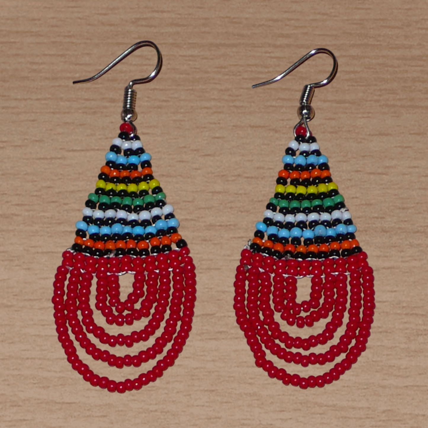 Boucles d'oreilles africaines rouges et multicolores en forme de gouttes. Elles mesurent 7 cm de long et 2,5 cm de large, et se portent sur des oreilles percées.