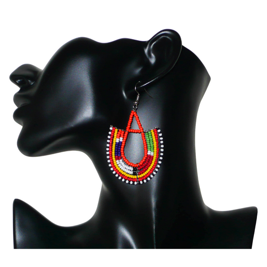 Boucles d'oreilles africaines traditionnelles aux couleurs et motifs ethniques Massai caractéristiques de l'artisanat kenyan. Elles se composent de perles de rocaille orange et multicolores fixées sur des structures en fils de fer en forme d'ancres. Ces boucles d'oreilles tribales mesurent 7.5 cm de long et 4.5 cm de large ; elles se portent avec des crochets en acier inoxydable sur des oreilles percées.