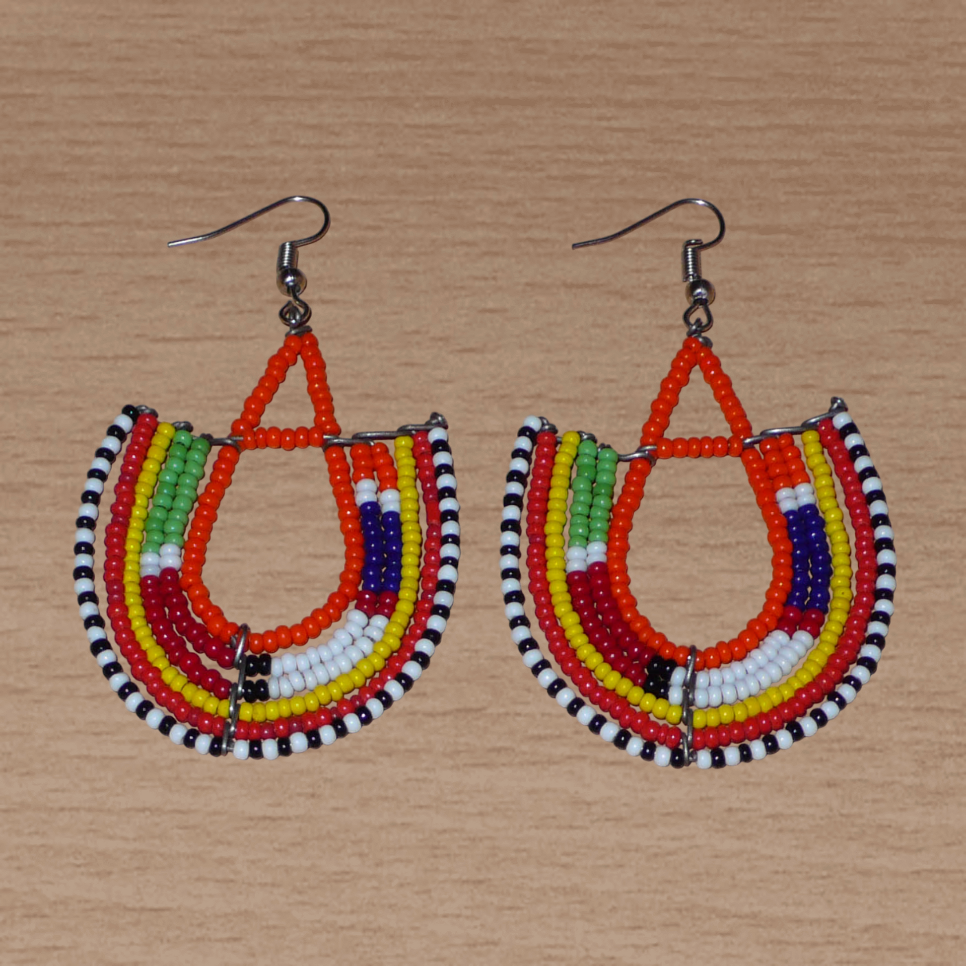 Boucles d'oreilles africaines traditionnelles aux couleurs et motifs ethniques Massai caractéristiques de l'artisanat kenyan. Elles se composent de perles de rocaille orange et multicolores fixées sur des structures en fils de fer en forme d'ancres. Ces boucles d'oreilles tribales mesurent 7.5 cm de long et 4.5 cm de large ; elles se portent avec des crochets en acier inoxydable sur des oreilles percées.