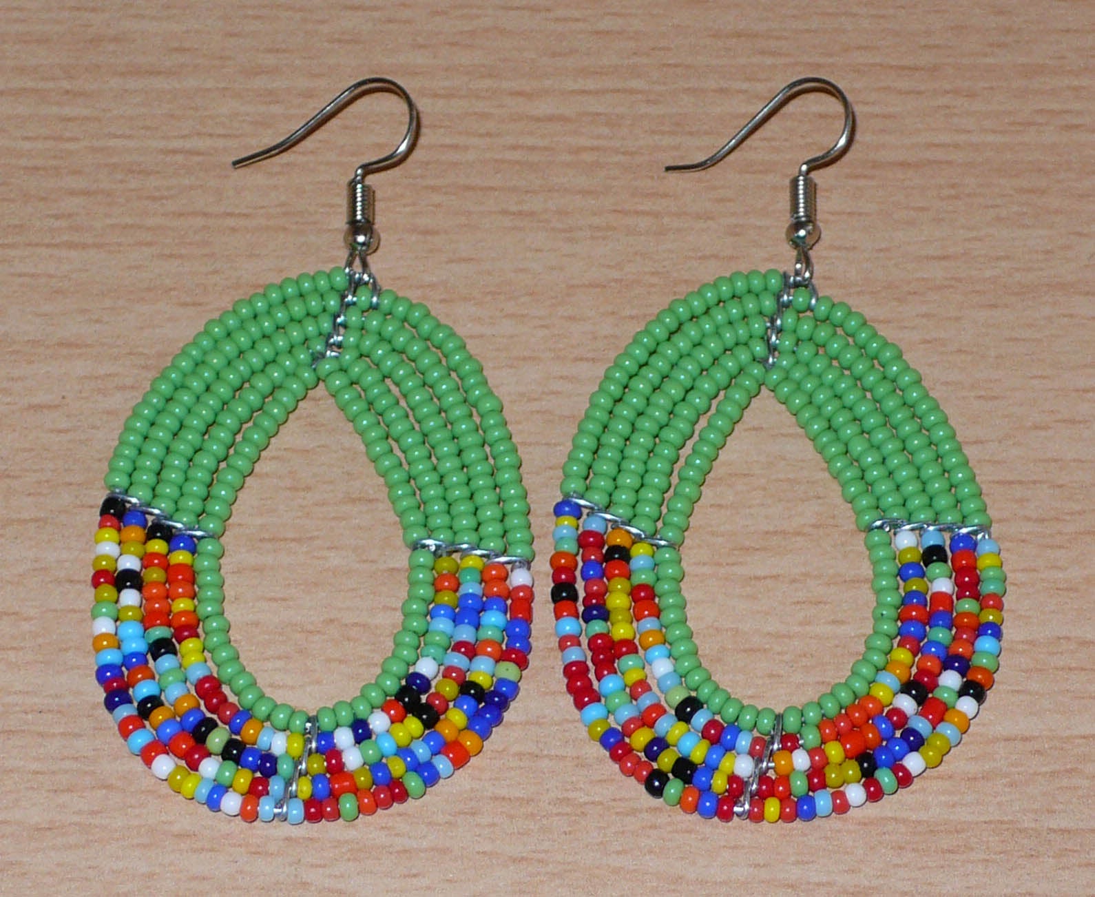 Boucles d'oreilles kenyanes multi-rangs vertes et multicolores en forme de gouttes. Elles mesurent 7 cm de long et 4 cm de large et se portent avec des crochets sur des oreilles percées.