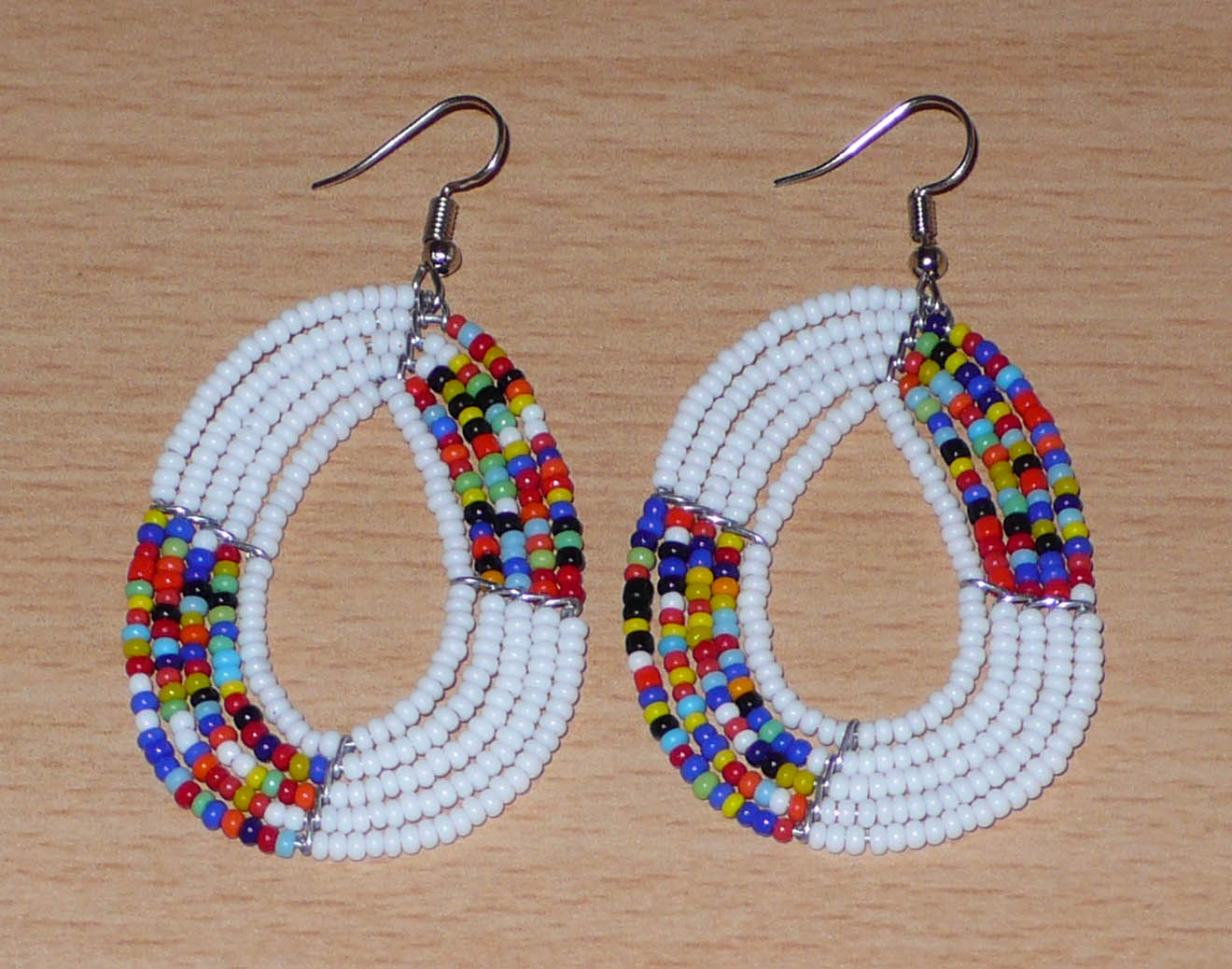 Boucles d'oreilles exotiques multi-rangs en forme de gouttes composées de perles de rocaille blanches et multicolores. De taille moyenne, elles mesurent 7 cm de long et 4 cm de large, et se portent sur des oreilles percées.