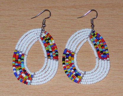 Boucles d'oreilles exotiques multi-rangs en forme de gouttes composées de perles de rocaille blanches et multicolores. De taille moyenne, elles mesurent 7 cm de long et 4 cm de large, et se portent sur des oreilles percées.