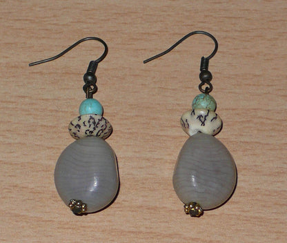 Boucles d'oreilles exotiques composées de perles et de graines de caniques grises. De taille moyenne, elles mesurent 5 cm de long et 1,5 cm de large, et se portent sur des oreilles percées.
