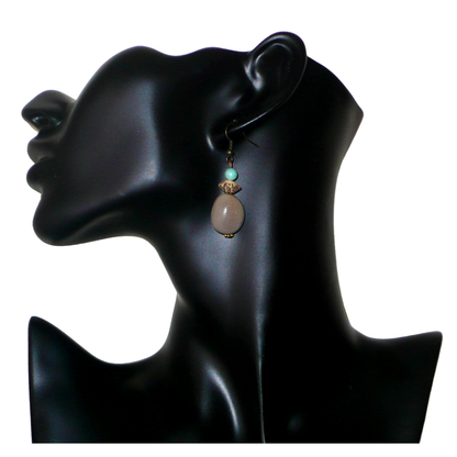 Boucles d'oreilles exotiques composées de perles et de graines de caniques grises. De taille moyenne, elles mesurent 5 cm de long et 1,5 cm de large, et se portent sur des oreilles percées.
