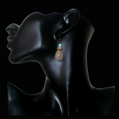 Boucles d'oreilles exotiques composées de perles et de graines de caniques grises. De taille moyenne, elles mesurent 5 cm de long et 1,5 cm de large, et se portent sur des oreilles percées.