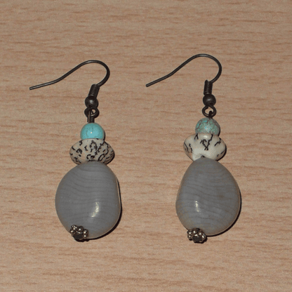 Boucles d'oreilles exotiques composées de perles et de graines de caniques grises. De taille moyenne, elles mesurent 5 cm de long et 1,5 cm de large, et se portent sur des oreilles percées.